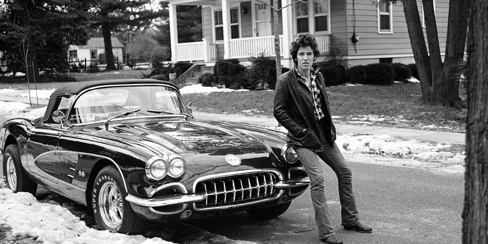 bruce springsteen posing in front of a corvette