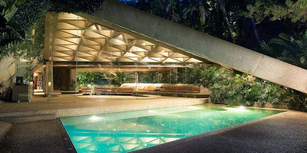 a mid-century modern house shaped like a triangle with a pool in front